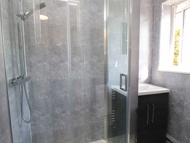 A bathroom with a glass shower enclosure and a sink with cabinet under a window at 11 Penygroes in Llanddeusant