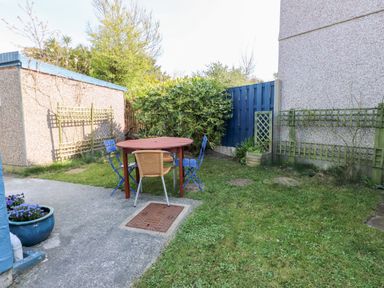 A garden area with a round table and three chairs on a concrete and grass surface at 11 Penygroes in Llanddeusant