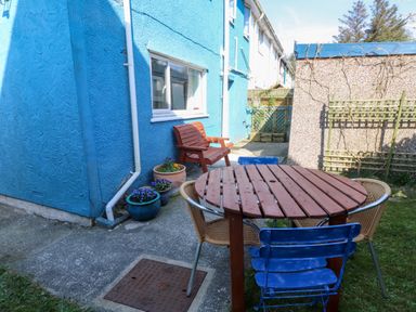 A small outdoor patio with a round wooden table surrounded by chairs and a small wooden bench against a blue painted wall at 11 Penygroes in Llanddeusant