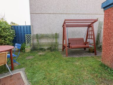 A garden area with a red wooden swing bench on a paved area and a wooden table with blue and wicker chairs at 11 Penygroes in Llanddeusant