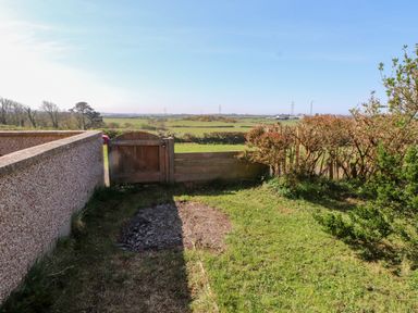 A small garden with a wooden gate and shrubs overlooking fields at 11 Penygroes in Llanddeusant