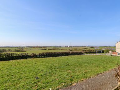A grassy backyard with a small swing set and houses in the distance at 11 Penygroes in Llanddeusant