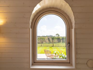 An arched window with a handle showing an outdoor view of a chair and fence at Andrus - Mayflower Meadow in Brandesburton
