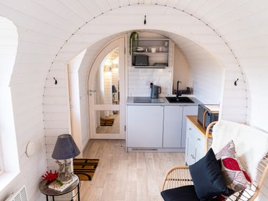 A small kitchen area with a sink, kettle, microwave, and chair inside a white wooden curved room at Andrus - Mayflower Meadow in Brandesburton