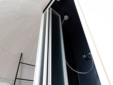 A shower area with a black shower panel and a metal showerhead inside a white paneled room at Andrus - Mayflower Meadow in Brandesburton