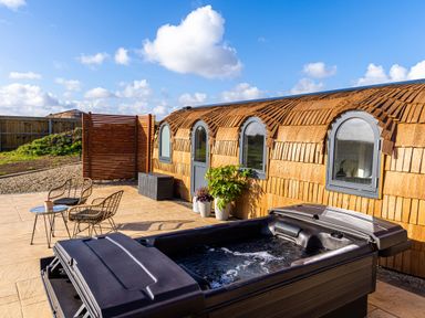 An outdoor patio with a hot tub rattan chairs a small table and a curved wooden building at Andrus - Mayflower Meadow in Brandesburton