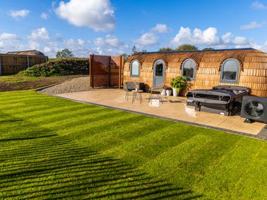 An outdoor area with two wooden pods a tiled patio two chairs a table and a hot tub at Andrus - Mayflower Meadow in Brandesburton