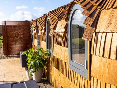 A wooden exterior wall with arched windows and potted plants on a tiled patio at Andrus - Mayflower Meadow in Brandesburton