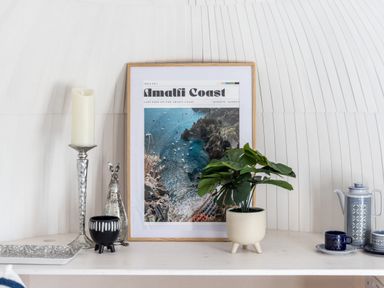 A shelf with a framed amalfi coast picture a candle holder a plant a silver rabbit ornament a black bowl and a blue and white tea set at Andrus - Mayflower Meadow in Brandesburton