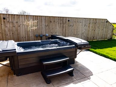 An outdoor hot tub with steps on a patio next to a wooden fence and grass at Andrus - Mayflower Meadow in Brandesburton