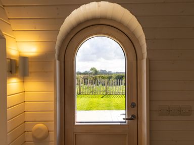 An arched wooden door with glass showing a garden and wooden fence at Indrek - Mayflower Meadow in Brandesburton