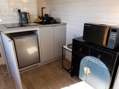 A kitchenette with a sink, electric kettle, small fridge, and microwave on a black cabinet at Indrek - Mayflower Meadow in Brandesburton