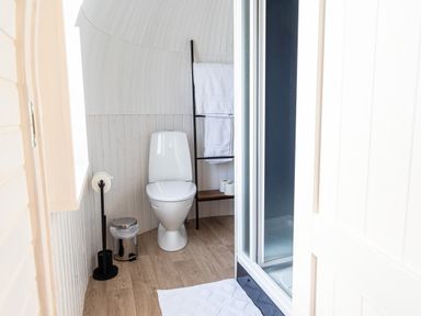 A bathroom with a white toilet towel rack with white towels shower with sliding doors and a white rug on wooden floor at Indrek - Mayflower Meadow in Brandesburton