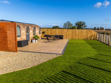 A patio with chairs and a table next to a wooden structure and a lawn at Indrek - Mayflower Meadow in Brandesburton