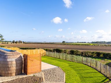 A garden with a grass lawn and wooden fencing overlooking plowed fields at Indrek - Mayflower Meadow in Brandesburton