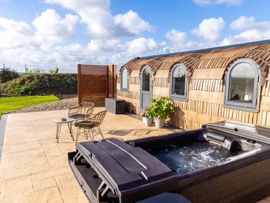 An outdoor patio with a hot tub two wicker chairs a small table and a wooden curved building at Indrek - Mayflower Meadow in Brandesburton
