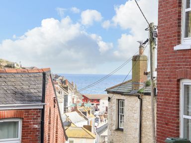 A view of rooftops and buildings overlooking the sea with a partly cloudy sky at Chy An Mor in Mevagissey
