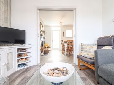 A living room with a television on a cabinet and a bowl of shells on a glass coffee table at Chy An Mor in Mevagissey
