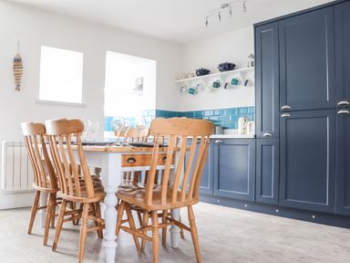 A kitchen with wooden chairs around a white table and blue cabinets and kitchenware at Chy An Mor in Mevagissey