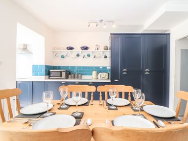 A dining table set with plates, cutlery, and glasses in a kitchen with blue cabinets and teal tile backsplash at Chy An Mor in Mevagissey