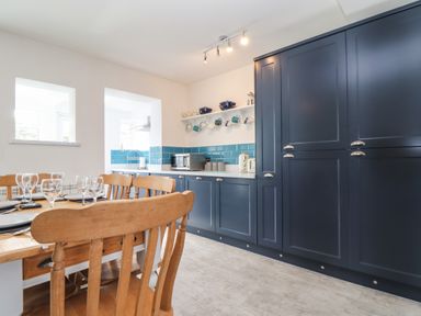 A kitchen with dark blue cabinets wooden dining chairs and a set dining table at Chy An Mor in Mevagissey