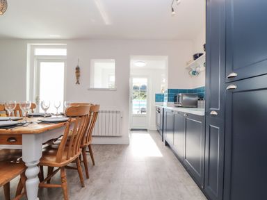 A kitchen with wooden dining table and chairs and blue cabinets at Chy An Mor in Mevagissey