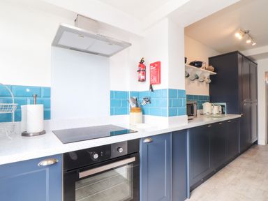 A kitchen with blue cabinets white countertop blue tiled backsplash stove and oven at Chy An Mor in Mevagissey