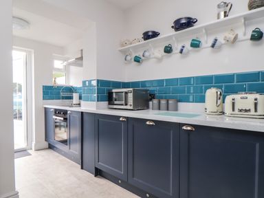 A kitchen with blue cabinets and tiles a microwave kettle toaster and mugs hanging at Chy An Mor in Mevagissey