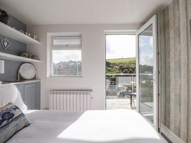 A bedroom with a bed pillow window radiator shelves and open balcony door showing outdoor view at Chy An Mor in Mevagissey