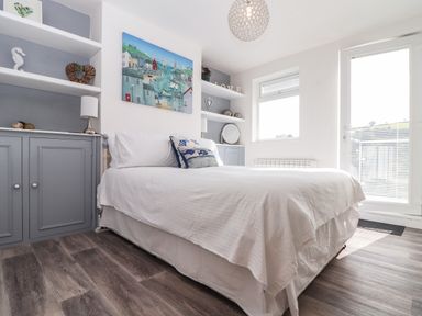 A bedroom with a bed white bedding built in shelving and cabinets and a door with window blinds at Chy An Mor in Mevagissey