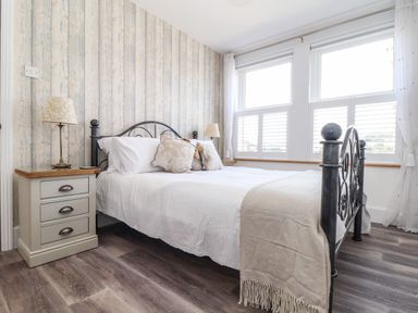 A bedroom with a metal framed bed two bedside tables and large windows at Chy An Mor in Mevagissey