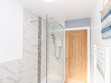 A bathroom with a shower enclosure wooden door and a towel radiator at Chy An Mor in Mevagissey