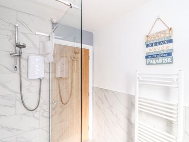 A bathroom with a shower area a glass shower screen a wooden door a towel radiator and a wall sign at Chy An Mor in Mevagissey