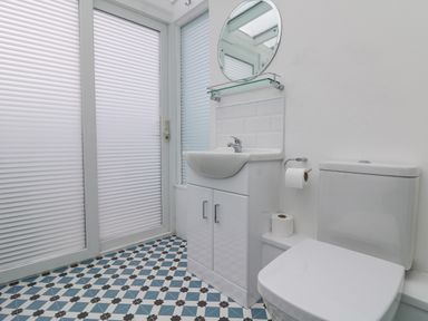 A bathroom with a toilet sink vanity mirror and patterned floor tiles at Chy An Mor in Mevagissey