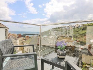 A balcony with two chairs and a table holding a pot of flowers overlooking rooftops and the sea at Chy An Mor in Mevagissey