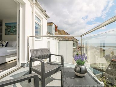 A balcony with two black chairs a black table and a vase with purple flowers overlooking rooftops and the sea at Chy An Mor in Mevagissey