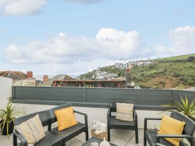 An outdoor patio with black chairs and cushions overlooking rooftops and hills at Chy An Mor in Mevagissey