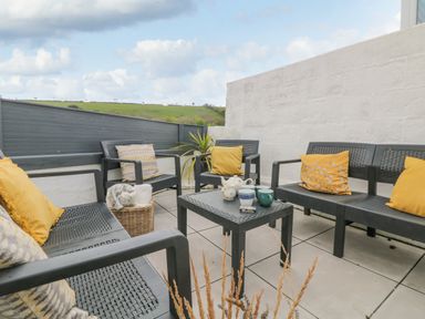 An outdoor patio area with black chairs and a table with cushions and a tea set at Chy An Mor in Mevagissey