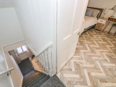 A staircase with carpeted steps and a handrail leading down next to an open door revealing a bedroom with patterned flooring at Chy An Mor Mevagissey
