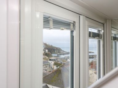 A view of rooftops and a coastal landscape through a window with white frames at Chy An Mor in Mevagissey