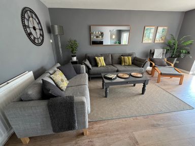 A living room with two sofas, a coffee table, a lounge chair, plants, wall clock, and framed pictures at Old Orchard in Saundersfoot