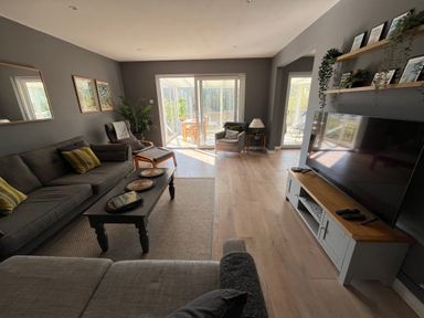 A living room with grey sofas a coffee table a TV on a stand and a glass door leading to a sunroom at Old Orchard in Saundersfoot