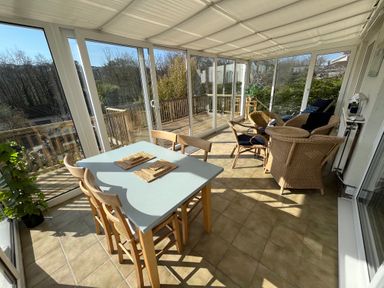 A sunroom with a dining table and chairs and wicker furniture with cushions at Old Orchard in Saundersfoot