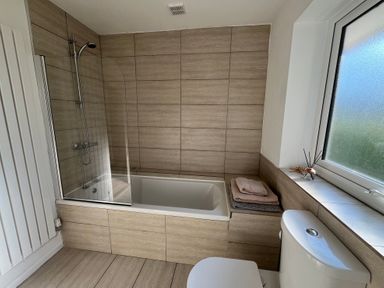 A bathroom with a bathtub shower combination next to a window and a toilet at Old Orchard in Saundersfoot