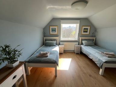A bedroom with two single beds each with a bedside table a window in the middle and a plant on a table at Old Orchard in Saundersfoot
