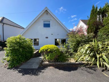 A white triangular house with bushes and plants in front at Old Orchard in Saundersfoot