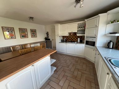 A kitchen with wooden dining table and chairs white cabinets and counters and wall art at Old Orchard in Saundersfoot