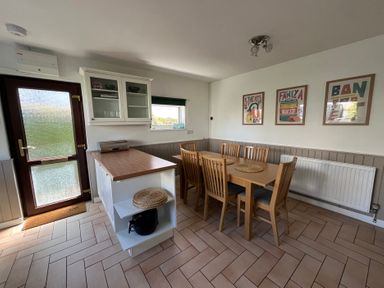 A dining area with a wooden table and six chairs next to a kitchen counter with shelves and a glass cabinet at Old Orchard in Saundersfoot