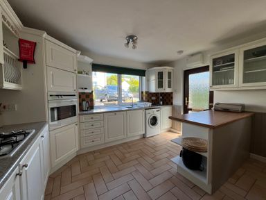 A kitchen with white cabinets a washing machine a gas stove and a window showing cars outside at Old Orchard in Saundersfoot