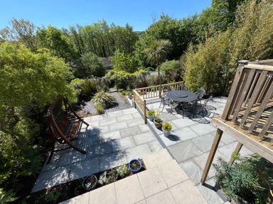 An outdoor patio area with a wooden swing bench a metal table with chairs potted plants and surrounding trees at Old Orchard in Saundersfoot